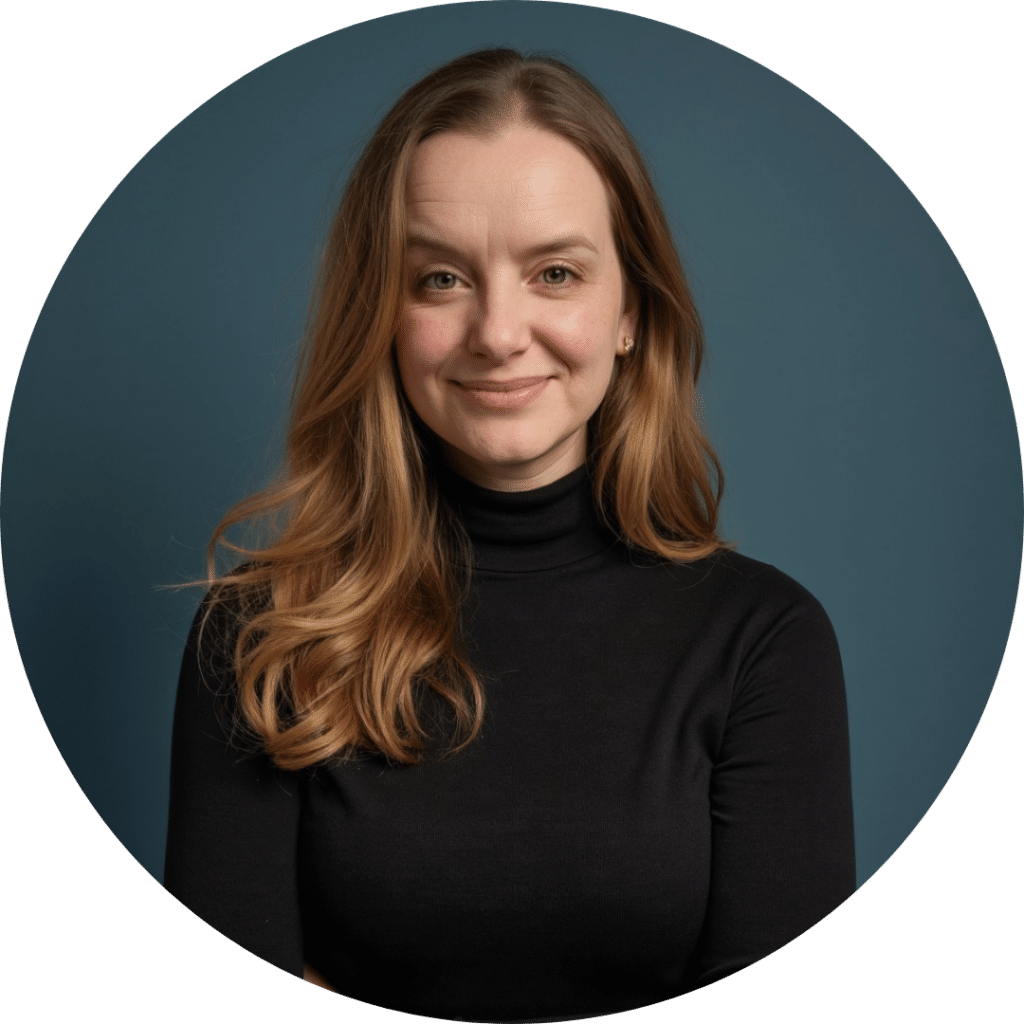 A woman with long, light brown hair wearing a black turtleneck stands against a plain blue background, smiling slightly with her arms crossed—reflecting the confidence that comes from providing quality care home health services.