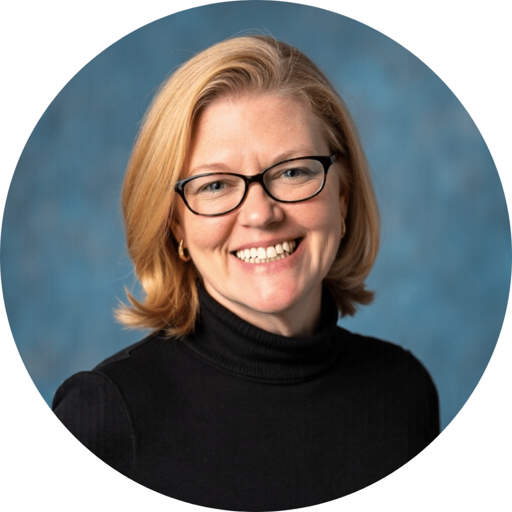 A woman with shoulder-length blonde hair, glasses, and a black turtleneck smiles in front of a blue background, reflecting the warmth and professionalism of quality care home health services.